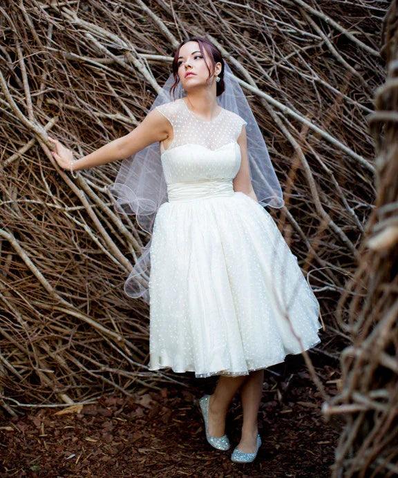 Bride in vintage-inspired polka dot wedding dress with veil, standing against rustic twig backdrop