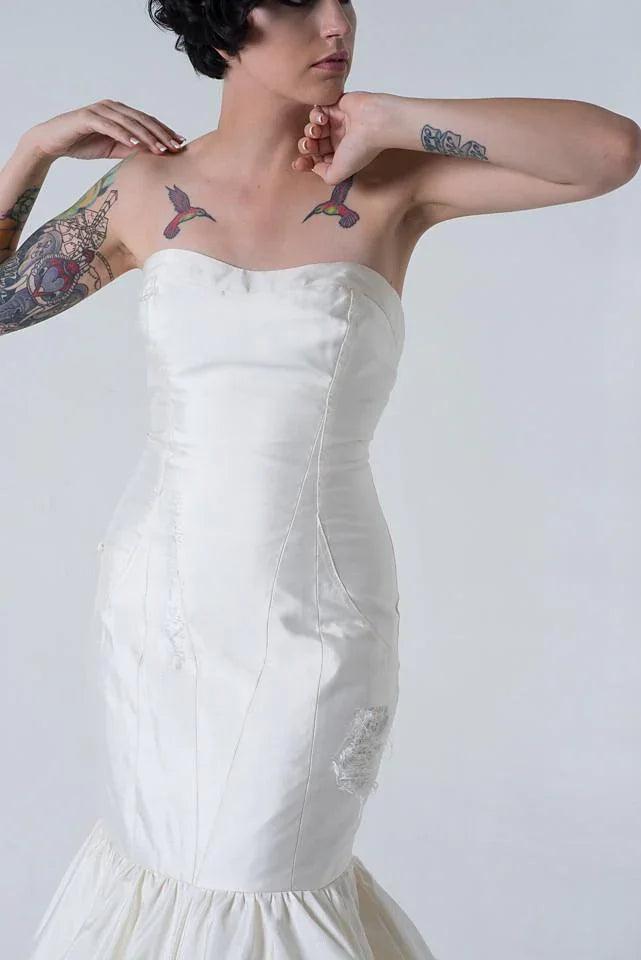 Strapless white wedding dress with lace details, worn by tattooed model for edgy bridal style