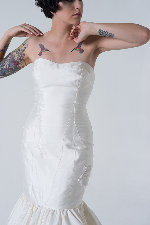 Strapless white wedding dress with distressed details, worn by tattooed model