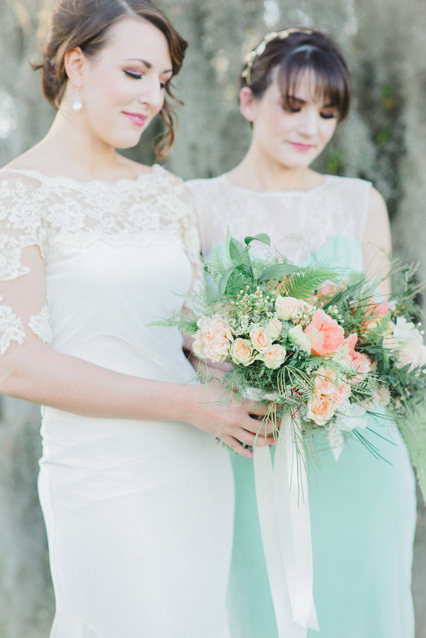 Bride in lace wedding dress holding bouquet with bridesmaid in mint dress